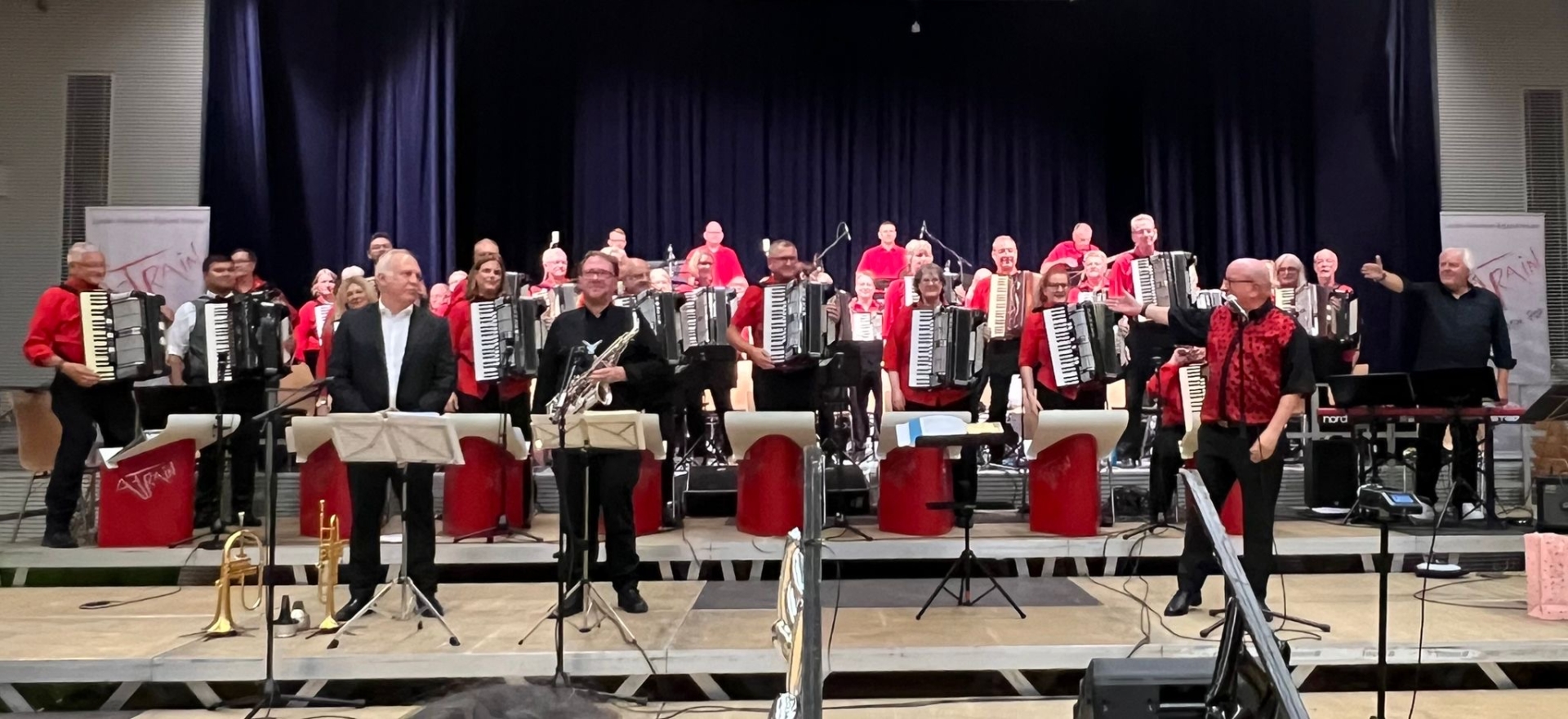 Die Band auf der Bühne, stehend. Vor der Band stehen Trompeter Stefan Klink und Saxofonist Prof. Matthias Anton. Rechts steht Bandleader Wolfgang Ruß und deutet auf die Band