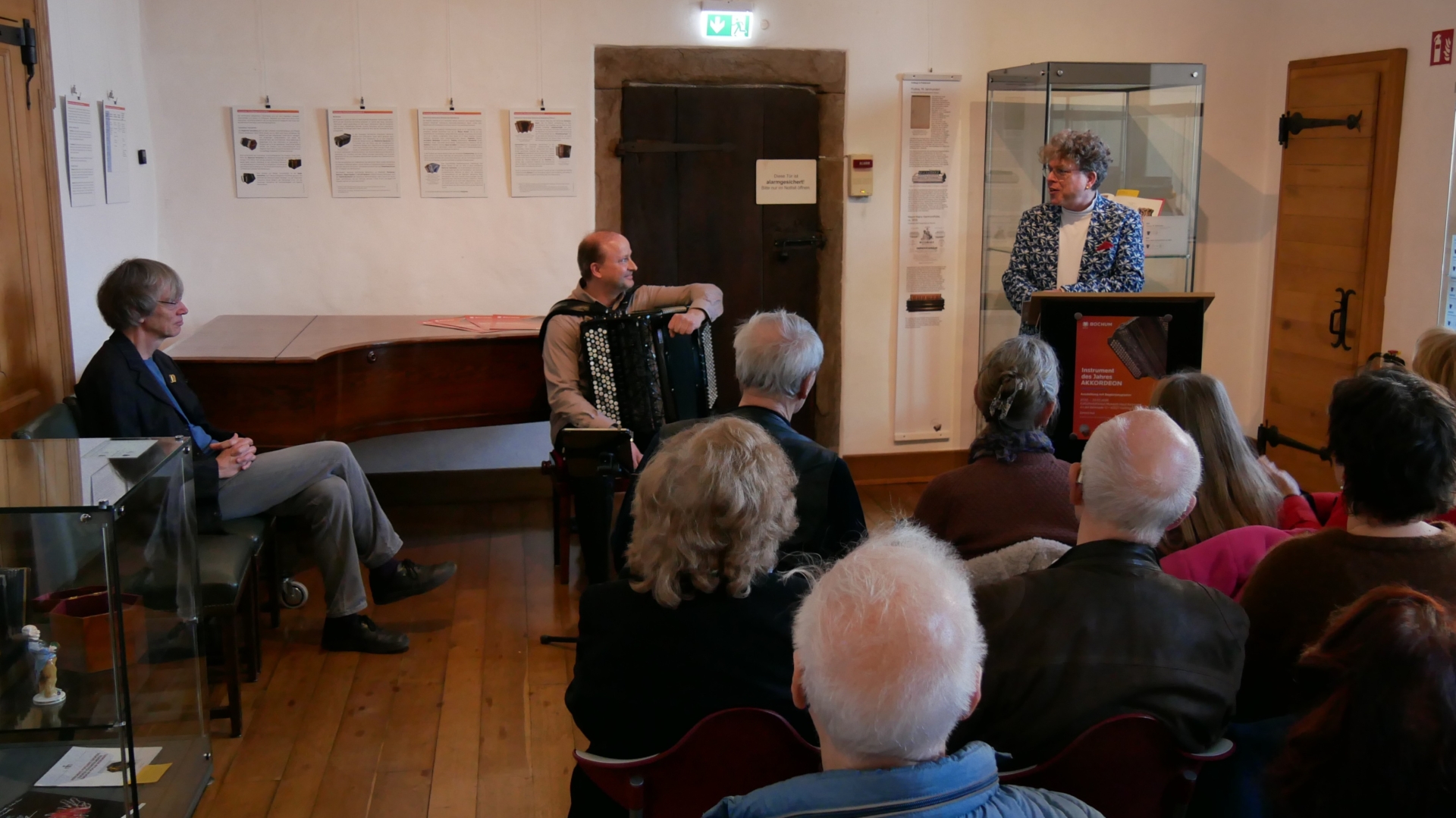 Im vollen Saal begrüßt Hausherr Christoph Schlierkamp die Gäste, links sitzt Organisator Ralf Kaupenjohann, in der Mitte Marko Kassl mit Akkordeon, der Vernissage musikalisch umrahmte.