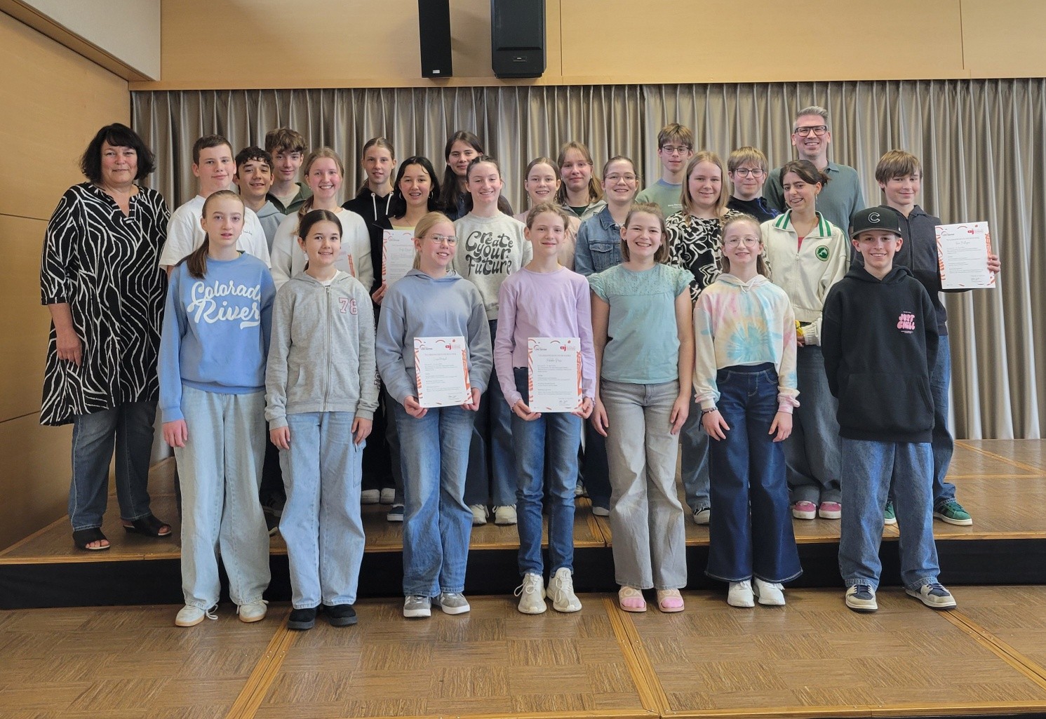 Die Kindern und Jugendlichen des Osterseminars stehen auf einer Bühne mit Urkunden in den Händen, begleitet von zwei Erwachsenen.