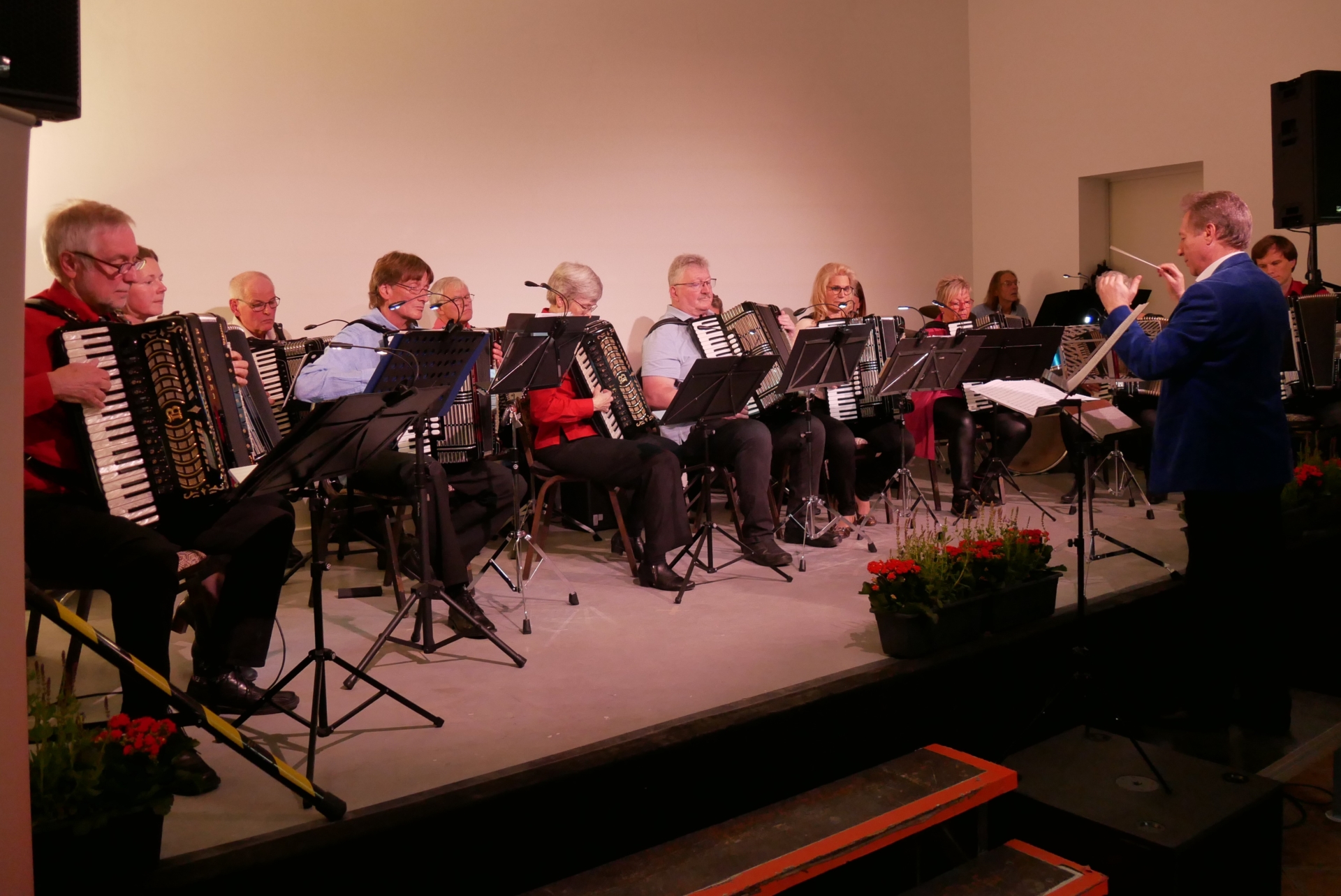 Das Akkordeon-Orchester sitzt auf der Bühne und spielt, davor Dirigent Pavel Schickmann.