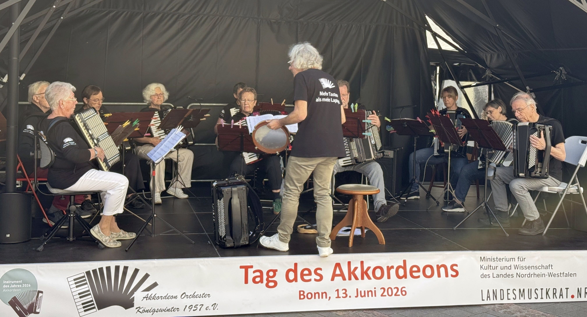 Die 10 Spieler des Akkordeon-Orchesters Königswinter auf der Bühne beim "Tag des Akkordeons" am 13. Juni 2026 in Bonn. Im Vordergrund: Dirigent Stefan Dörrenbächer mit Tambourin.